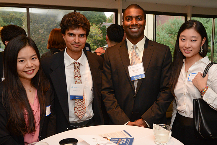 Two Brandeis students and two alumni stand together at a career fair.