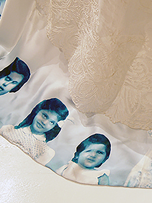 close up of white marriage turban piece train area that has blue images of children and one woman around the bottom edge of the skirt. French lace is draped over the bottom layer of the garment.