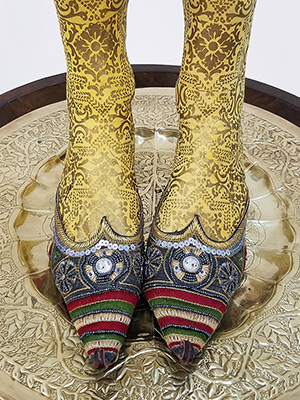 view of the sculpture showing the pointed shoes and yellow legs on top of a gold engraved tray