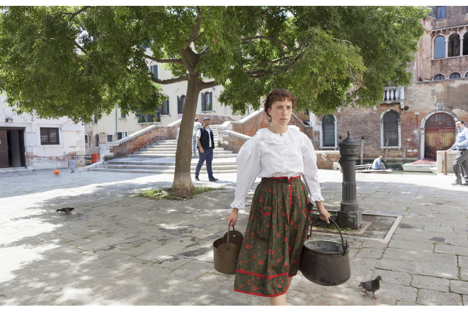 woman carrying buckets through the streets, men looking on