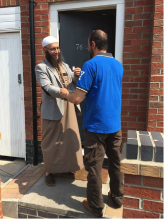 A member of “Muslim Moves” hands a recent French émigré the key to his new house in the UK.