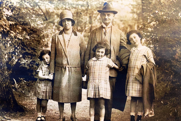 A black and white photo showing a family in the early 1900s consisting of two parents and three small children standing outdoors on a path among trees
