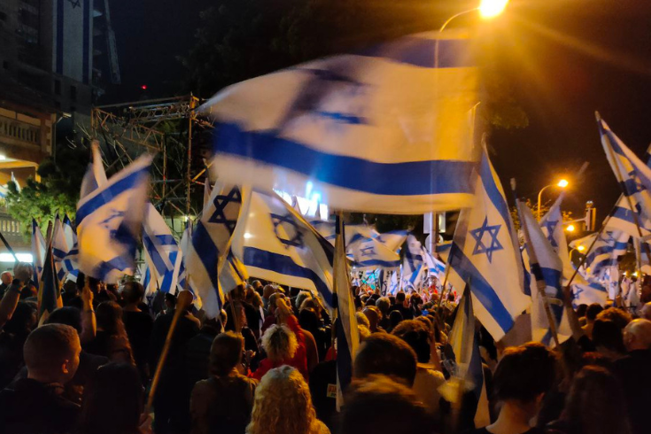 Photo of Israeli protest; people with Israeli flags at night rally