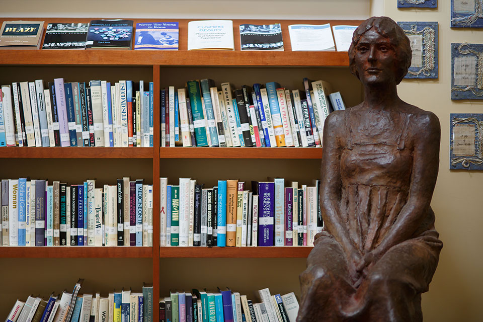 A statue of a woman sitting in front of a bookshelf full of books