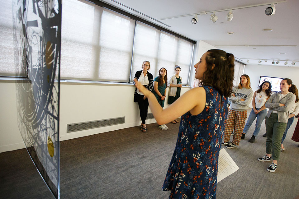 Students look on as a person talks about a piece of art