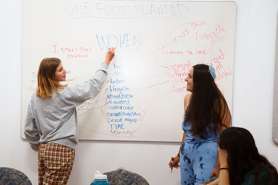 Two students stand at a whiteboard with writing on it