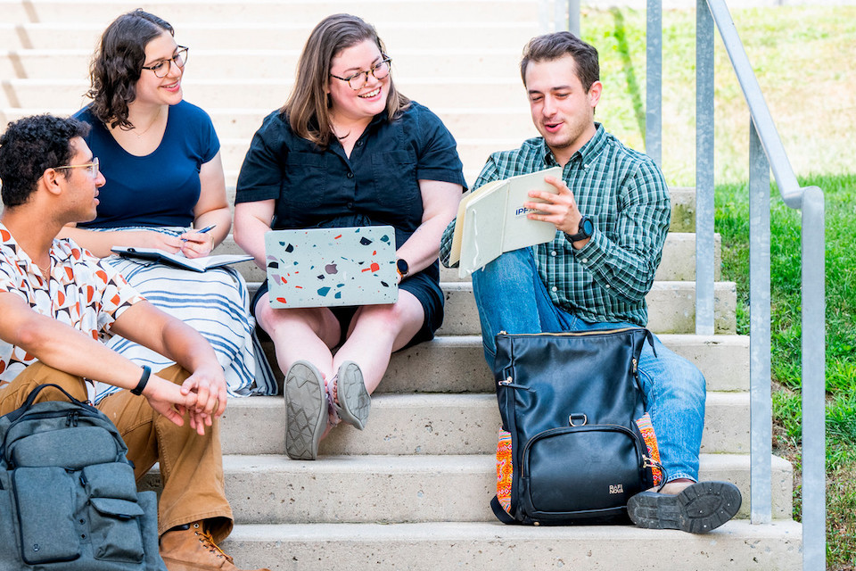 Students sit on the steps outside a building on the Brandeis campus