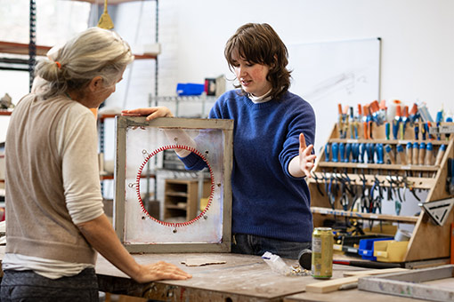 A student and professor talk in an art studio during a sculpture class