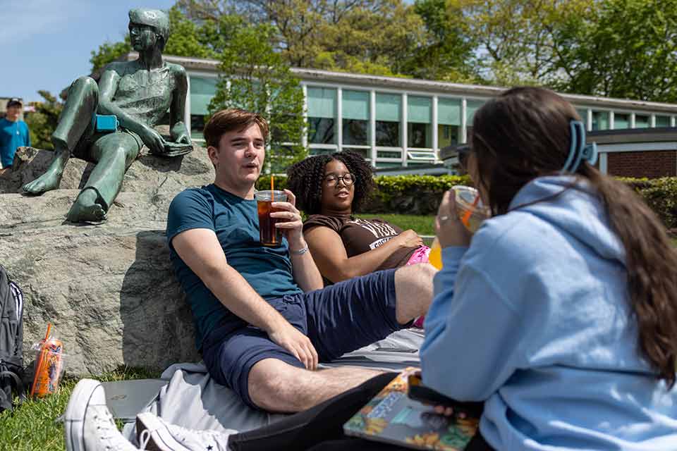 Three students on campus, seated by a statue
