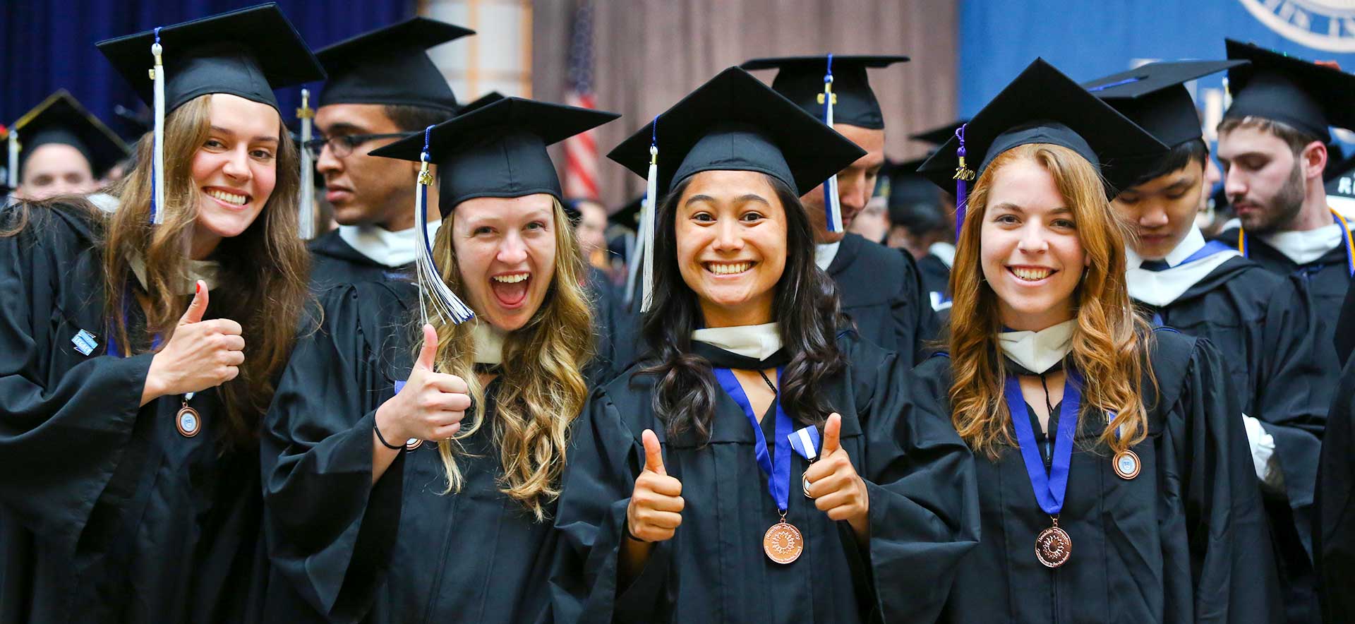 Brandeis graduates in caps and gowns giving the thumbs up