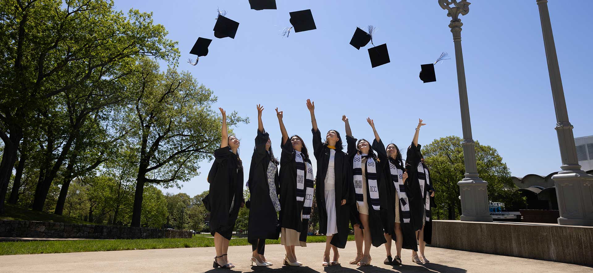 Students dressed in commencement regalia throwing their caps in the air. 
