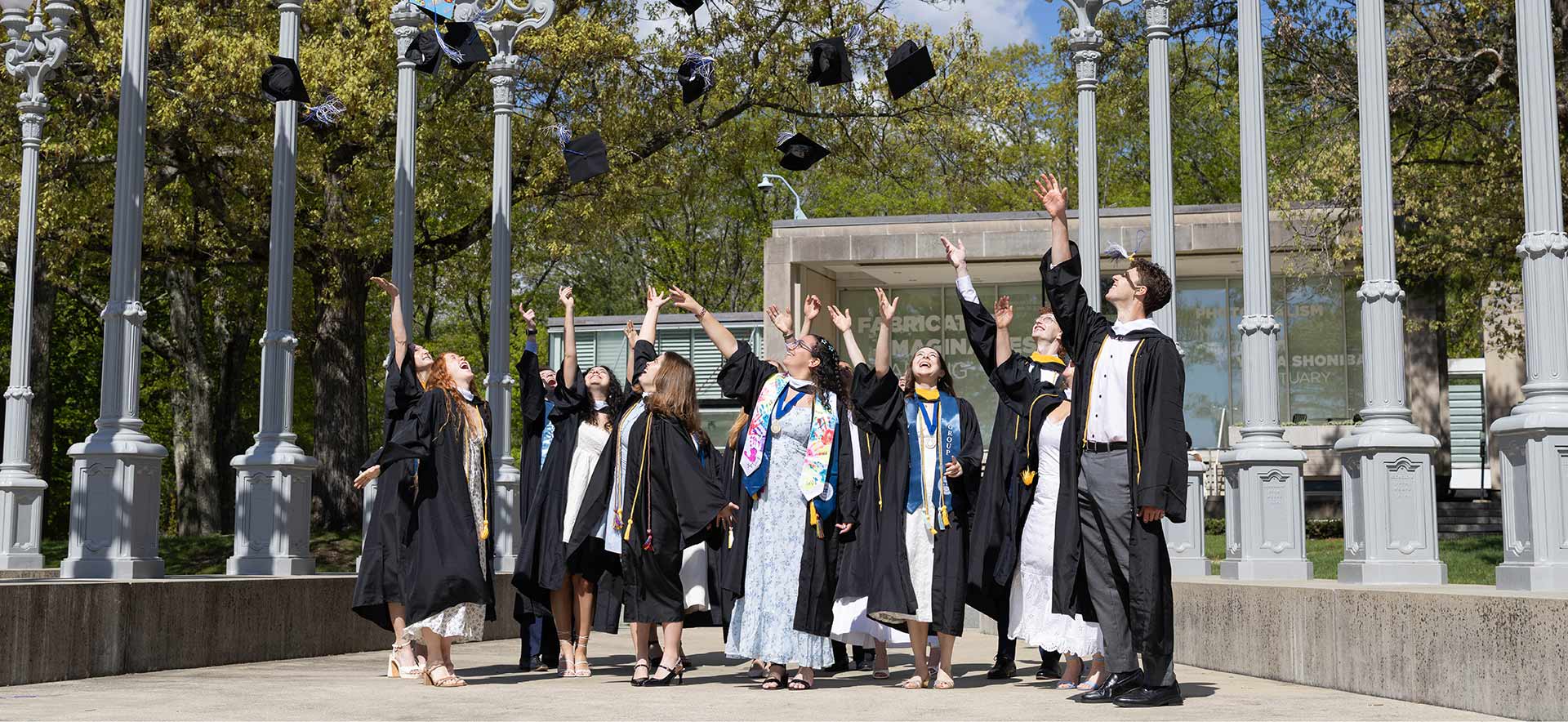Students dressed in commencement regalia throwing their caps in the air. 