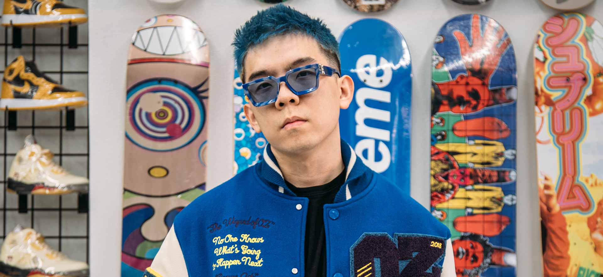 Jiahuan Green Xia with blue hair and sunglasses in front of a wall of sneakers and skateboards