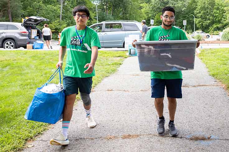 Two students in green shirts carrying items