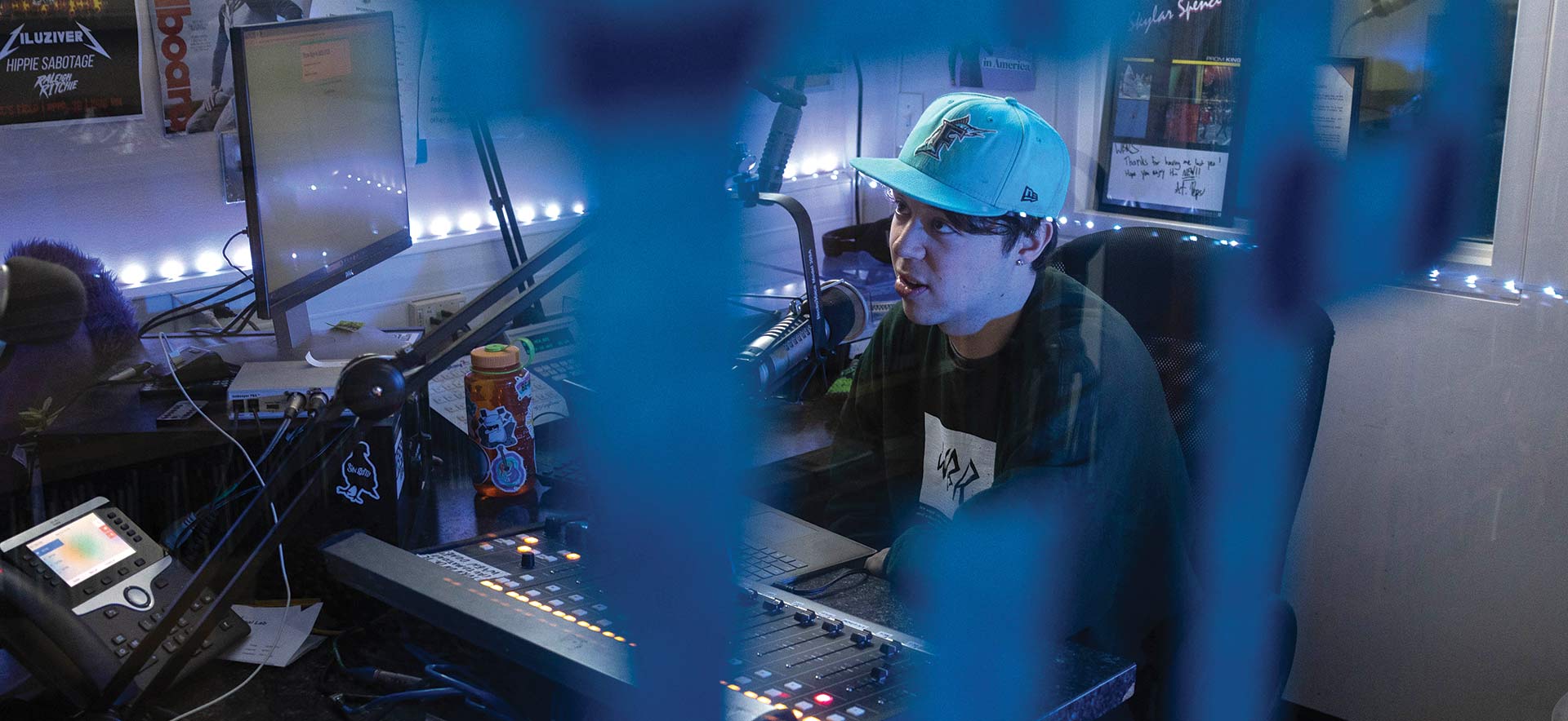 A person with a blue hat speaks into a microphone inside a radio station