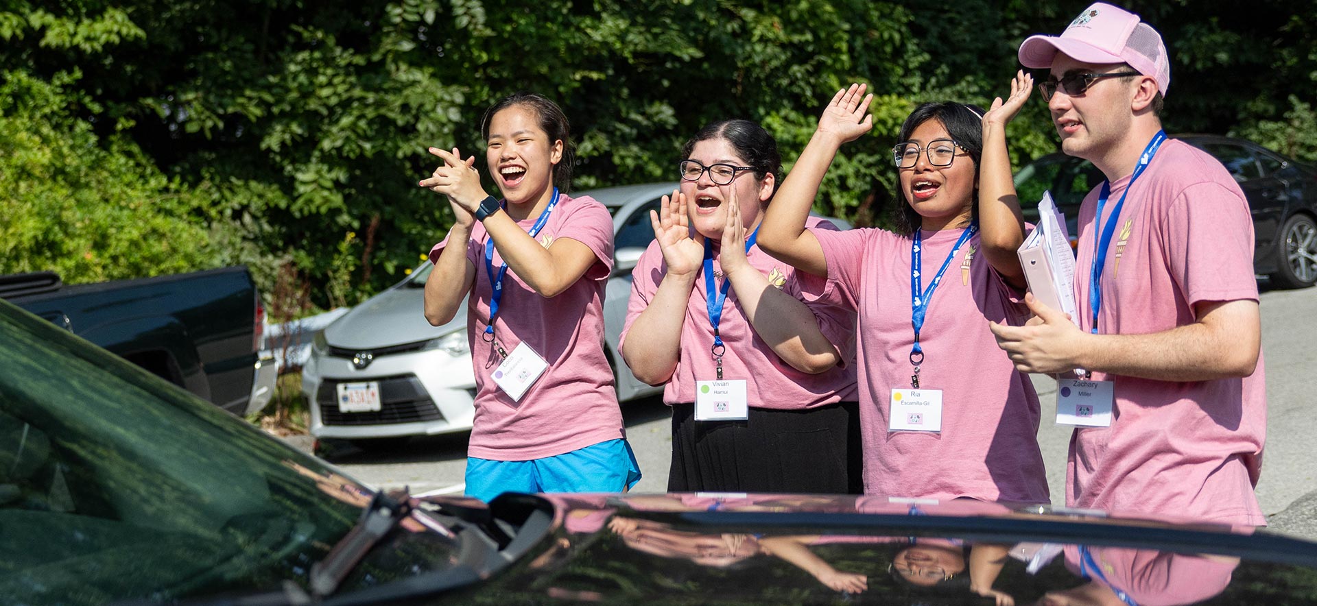 Four students in pink t-shirts smiling and cheering during move in.