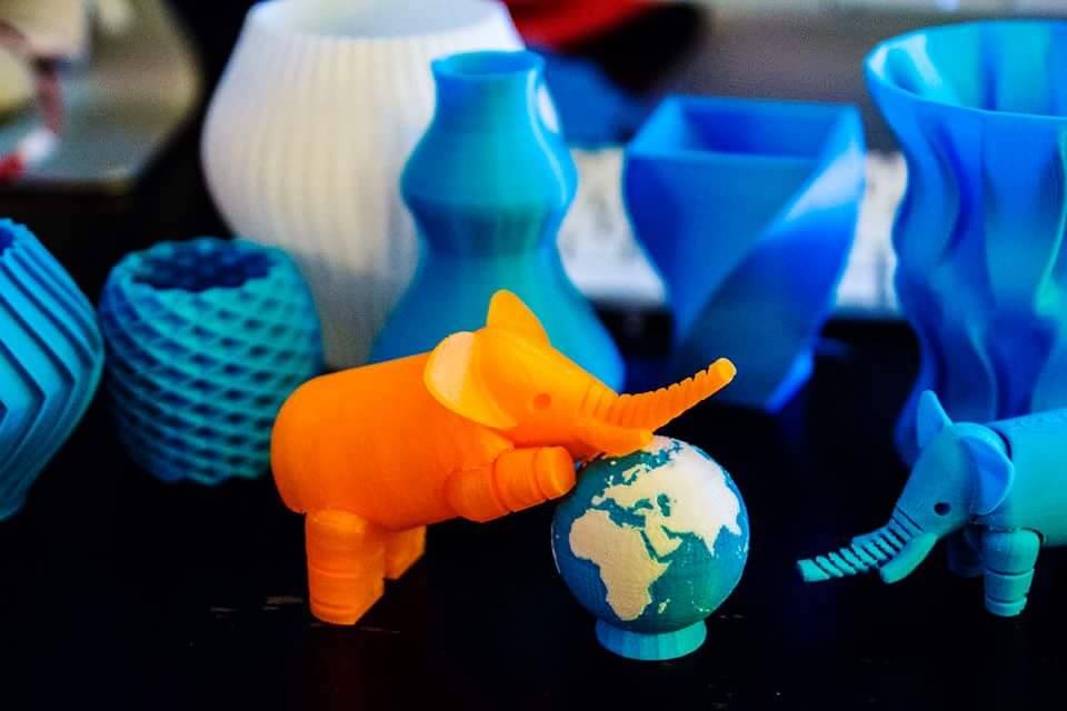 A 3D printed orange elephant leans on a 3d printed globe