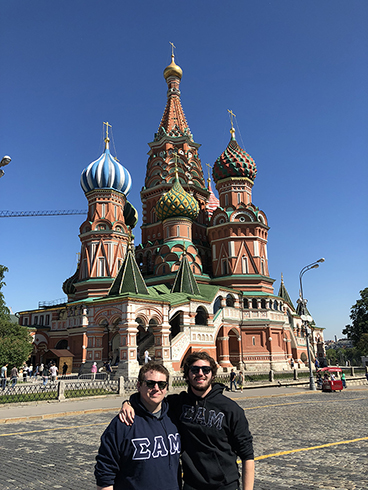 2 Students standing in front of Saint Basil's Cathedral in Moscow, Russiaoking at papers; on the wall behind her is a map of South America covered with green hand prints