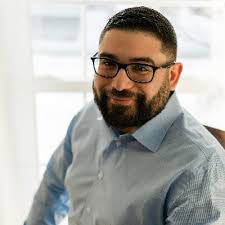 Young man with beard and glasses, smiling.