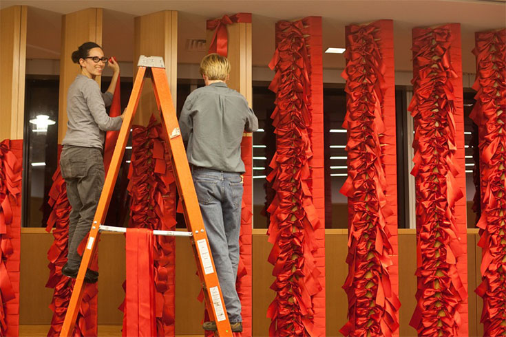 Nelly Agassi creating an installation, on a ladder with and assistant helping