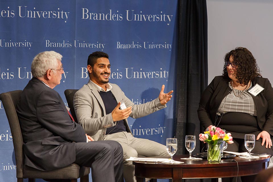 Three speakers seated on a stage, in animated discussion. 