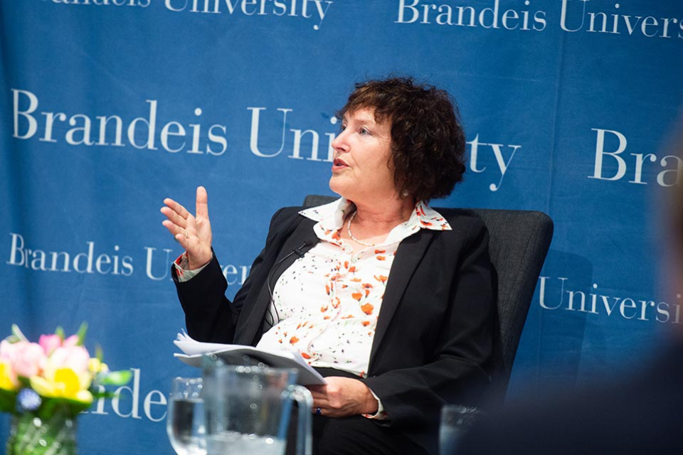 Karnit Flug is seated on stage, gesturing thoughtfully as she speaks. 