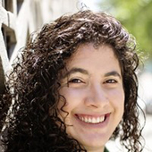 Young woman with black curly hair looks off-camera, with a Brandeis University logo banner behind her.