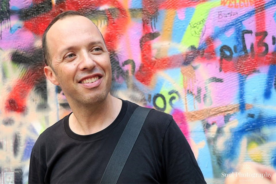 man smiling in front of a colorful mural