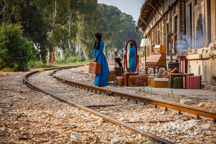 Woman stands with suitcase next to railroad tracks