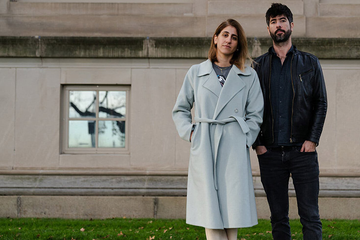 Sally Abed and Alan-Lee Green standing side by side outdoors, on grass, in front of a building.