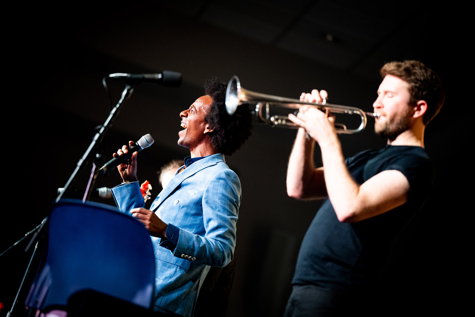Man singing into a microphone while another plays the trumpet