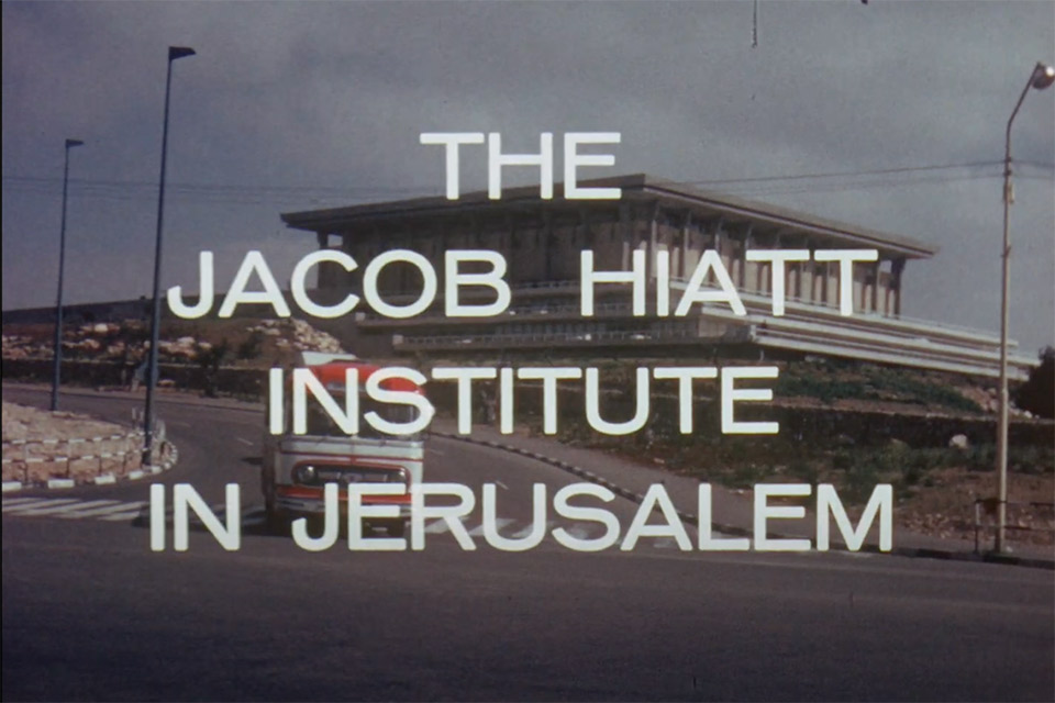 A red 1960s-era bus drives down a road, the Israeli Knesset (Parliament) building behind it. Superimposed on the image are the words: The Jacob Hiatt Institute in Jerusalem