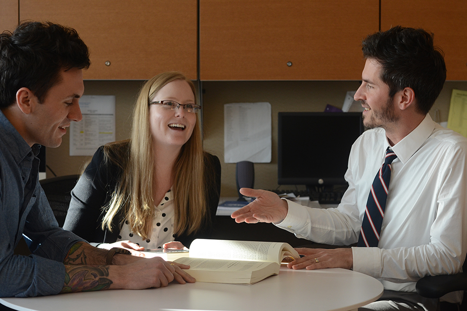 Three scholars – two men and one woman – sitting at a table, engaged in animated discussion