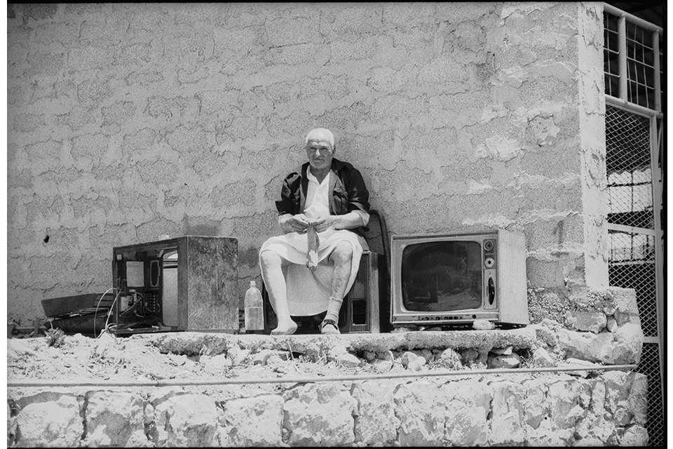 Man seated in front of a stone wall, putting on socks