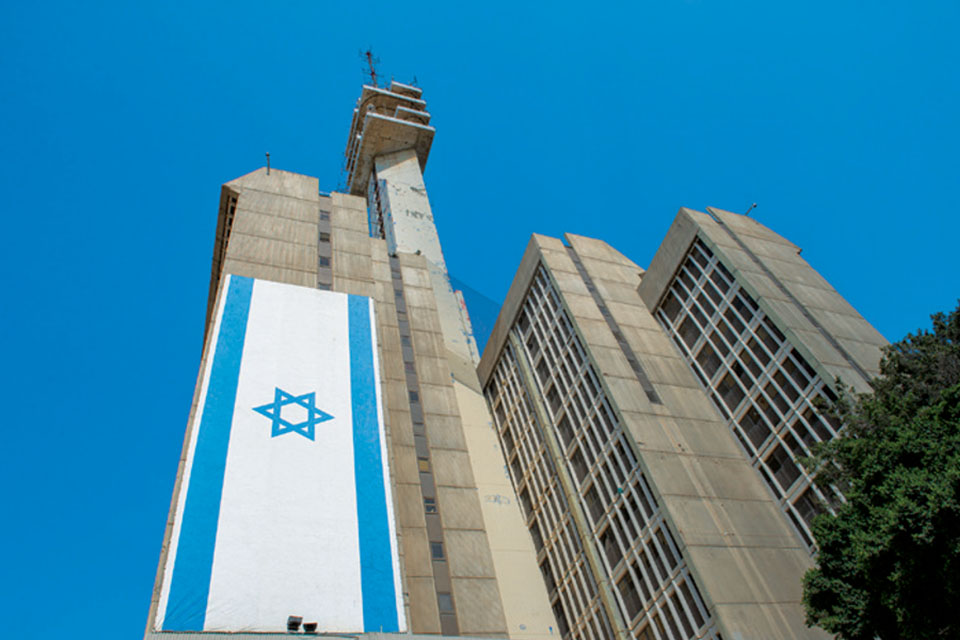 Tall, gray building with a long Israeli flag hanging vertically down one wall