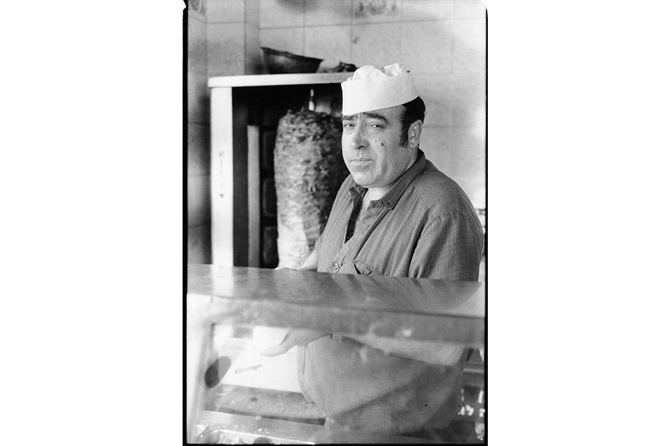 A man behind a counter, next to a schwarma spit 
