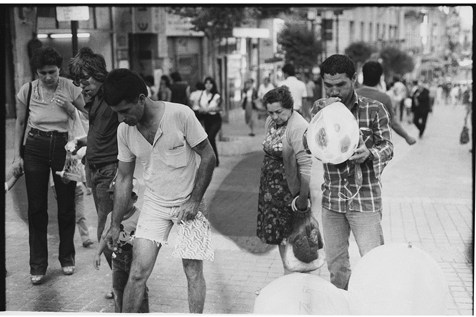 A man blows up a balloon, while other people stand nearby