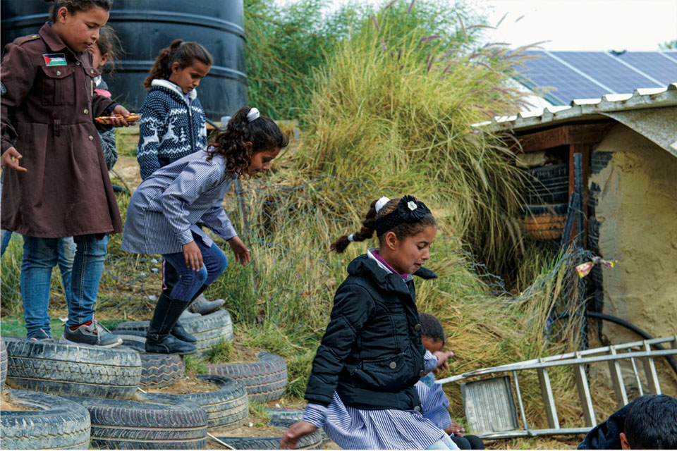 Children jumping off tires placed horizontally on the dirt