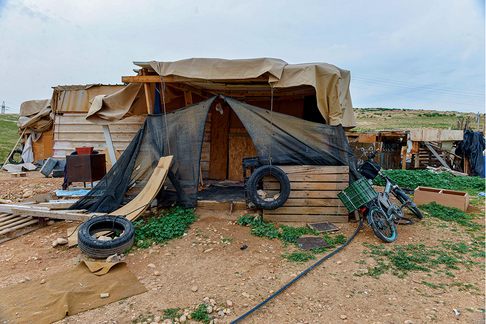 Makeshift structure with tarps, wood boards, tires, and assorted junk