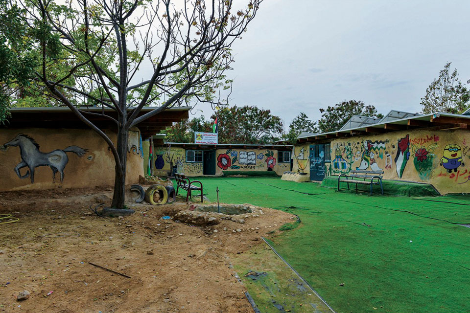 Art covers the walls of three low buildings around a grassy courtyard 