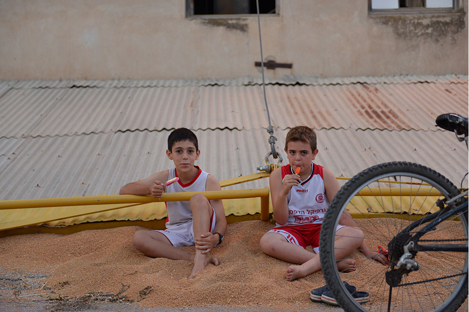 Two boys sitting in orange-hued, sandy substance, eating popsicles