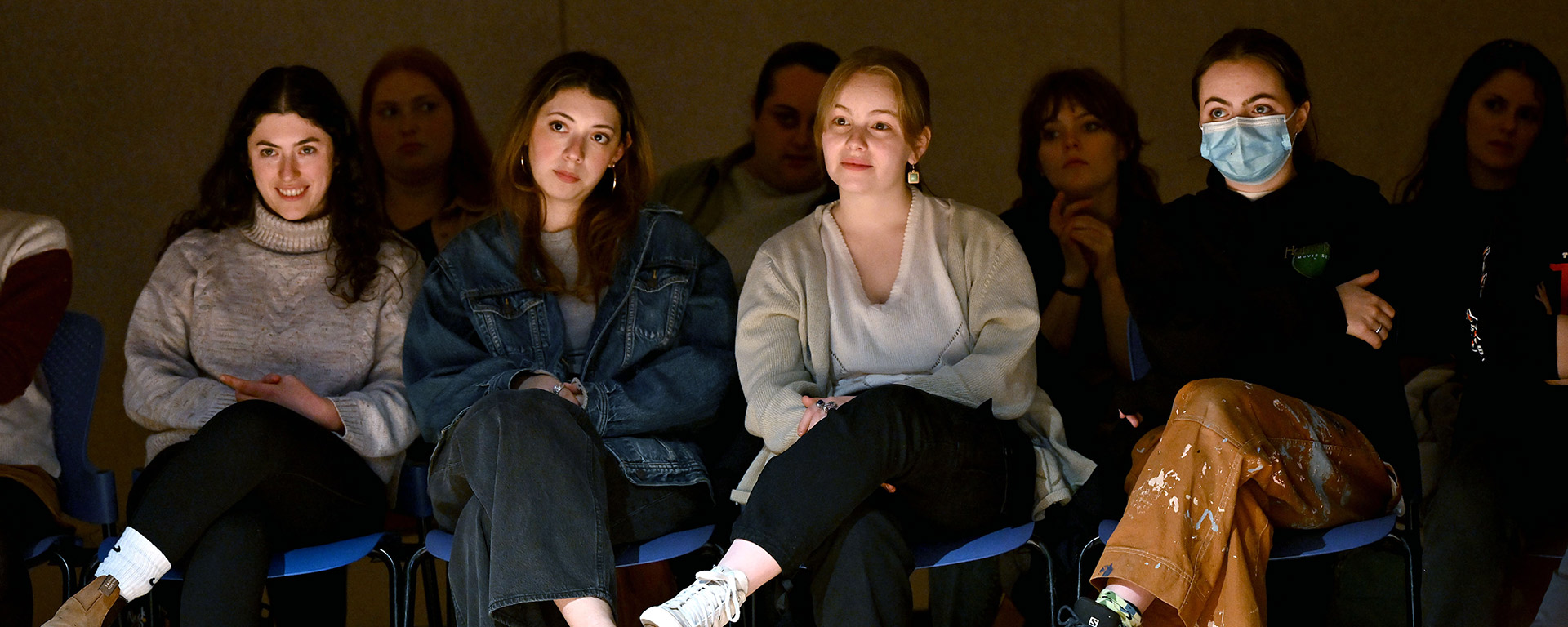 Students seated in the front row of an audience, watching unseen performers with a variety of engaged expressions