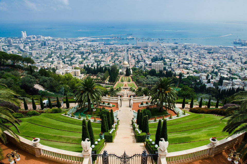 Aerial image of stepped garden leading down to view of city buildings and beyond them, the blue sea.