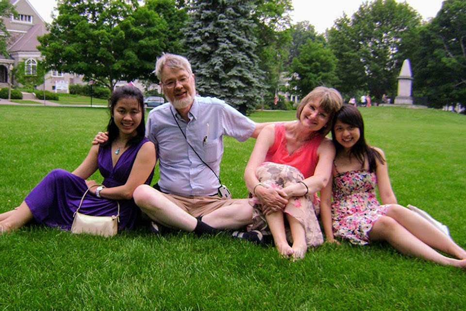 Staff and students smiling and sitting on grass outside.