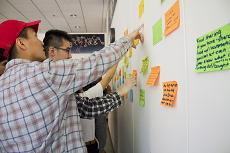 two students working at whiteboard full of stickies