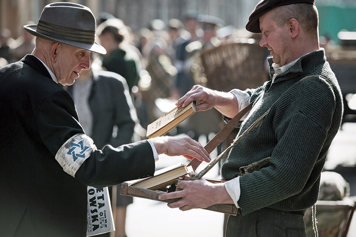 two men looking over books. one man wears a white armband with a blue Star of David