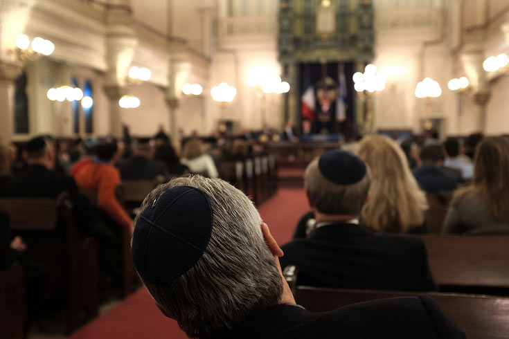 A man with a yarmulke in temple, leaning over to see the altar