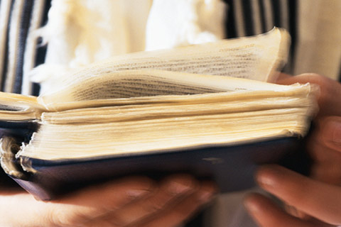 A man in religious clothing holds an ancient textbook