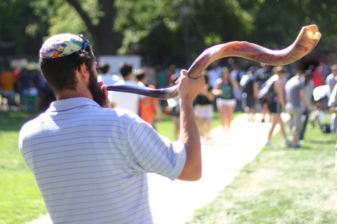 A rabbi blowing a shofar outside with his congregation