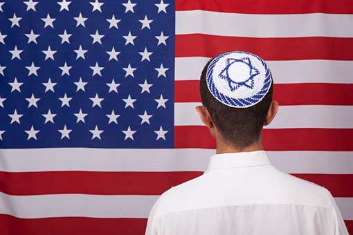 A man with a yarmulke stands before an American flag